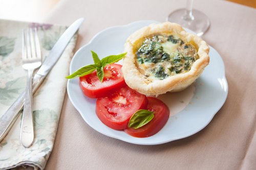 A savory spinach quiche in a pastry shell, served with fresh tomato slices and basil on a light blue plate.