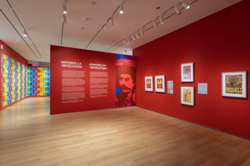 Art gallery interior featuring vibrant red walls, colorful artwork, and informational panels about revolution.