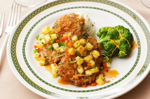 A plate of breaded chicken topped with pineapple salsa, served with mashed potatoes and steamed broccoli.
