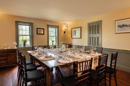 A cozy dining room set for a meal, featuring a large table with elegant tableware and wooden chairs.