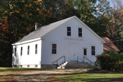 A white, single-story town house with steps, surrounded by trees in autumn foliage.