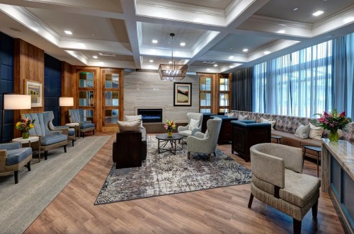 Modern lounge with comfortable seating, a fireplace, and large windows, featuring floral arrangements and warm lighting.