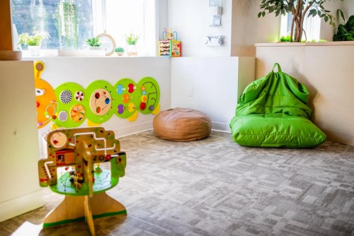 A bright playroom with a colorful wall, a wooden activity tree, green bean bags, and a cozy atmosphere.