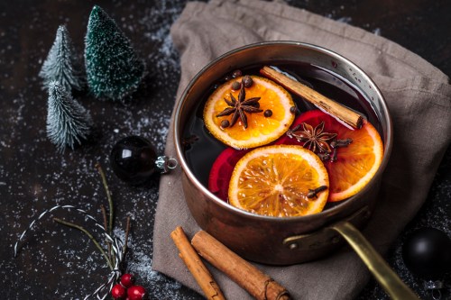A pot of spiced mulled wine with orange slices, cinnamon sticks, and star anise, surrounded by festive decorations.