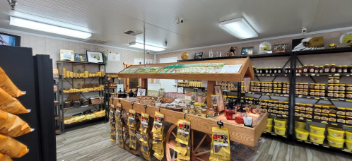 A cozy shop interior featuring shelves of honey products, a wooden display stand, and various jars and bottles.