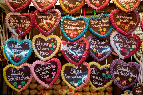 Colorful heart-shaped gingerbread cookies with various German phrases and decorations hanging in a festive display.