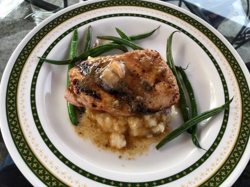 Grilled salmon fillet topped with sauce, served with mashed potatoes and green beans on a decorative plate.