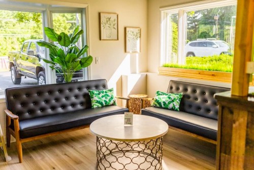 Cozy seating area with black sofas, green cushions, a round table, and large windows letting in natural light.