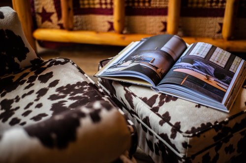 A cowhide-patterned chair and ottoman with an open book showcasing interior design images on a rustic background.