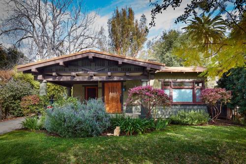A charming green bungalow surrounded by lush gardens and colorful flowers under a clear blue sky.