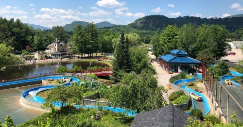 A scenic view of a water park with winding slides, surrounded by lush greenery and mountains under a blue sky.