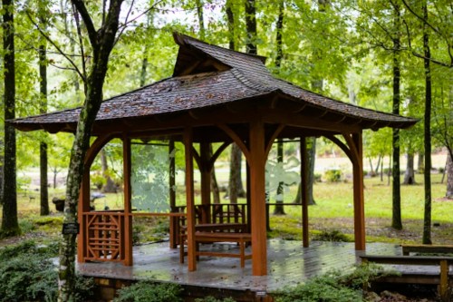 A wooden gazebo surrounded by lush green trees in a serene outdoor setting.