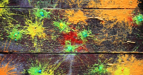 Colorful splatters of paint in yellow, green, and orange on a dark wooden surface, creating an abstract design.