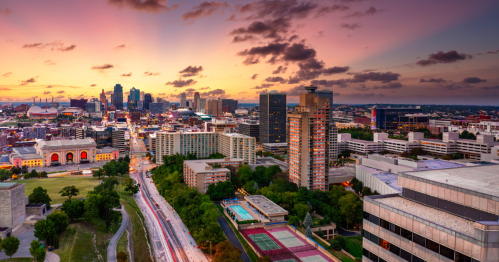 A vibrant city skyline at sunset, featuring buildings, roads, and a colorful sky with clouds.