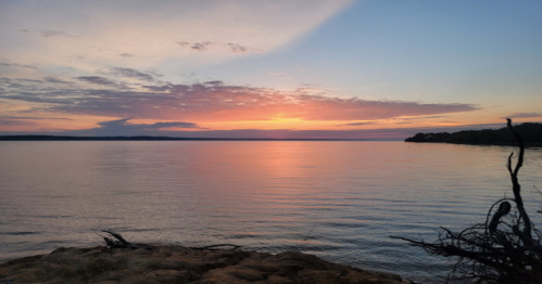 A serene sunset over a calm lake, with colorful clouds reflecting on the water's surface.