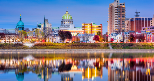 City skyline at dusk, featuring historic buildings and modern architecture reflected in a calm river.