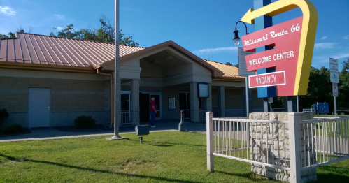A welcome center on Route 66 with a bright sign indicating vacancy, surrounded by green grass and a clear blue sky.