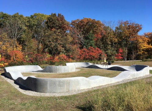A curved concrete structure in a park, surrounded by colorful autumn trees and a clear blue sky.