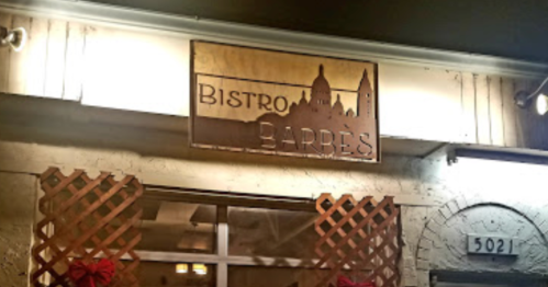Sign for "Bistro Barbes" with a silhouette of a cityscape, illuminated at night. Decorative lattice in front.