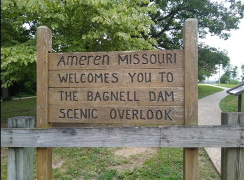 Wooden sign reading "Ameren Missouri welcomes you to the Bagnell Dam Scenic Overlook" in a natural setting.