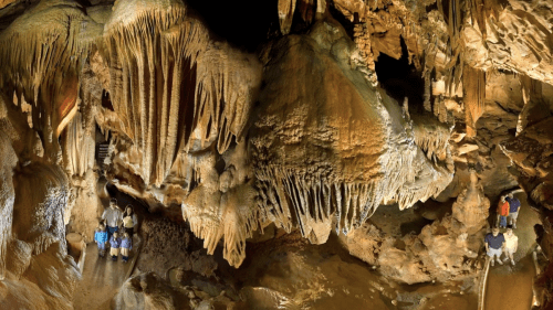 A panoramic view of a cave with impressive stalactites and stalagmites, featuring visitors exploring the underground landscape.