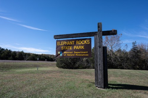Sign for Elephant Rocks State Park in Missouri, with a clear blue sky and grassy area in the background.
