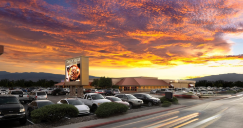 A restaurant with a large sign, surrounded by parked cars, under a vibrant sunset sky.