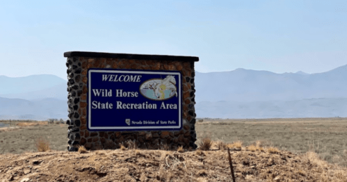 Welcome sign for Wild Horse State Recreation Area, with mountains in the background and a clear blue sky.