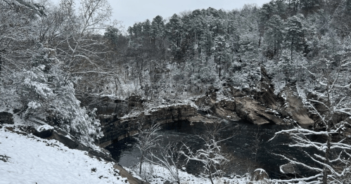 A snowy landscape featuring a river surrounded by rocky cliffs and trees, creating a serene winter scene.