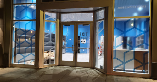 Entrance to a museum with blue walls and geometric window designs, featuring an exit sign.