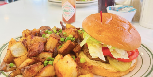 A juicy burger with lettuce, tomato, and pickles, served with crispy golden-brown potato cubes on a plate.