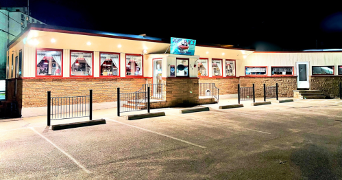 A brightly lit restaurant at night with large windows and a parking lot, featuring a sign that reads "Pork Place."