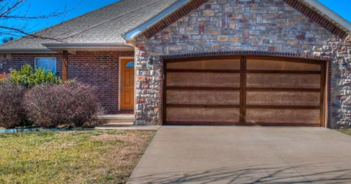 A brick and stone house with a wooden garage door and a well-maintained lawn on a sunny day.