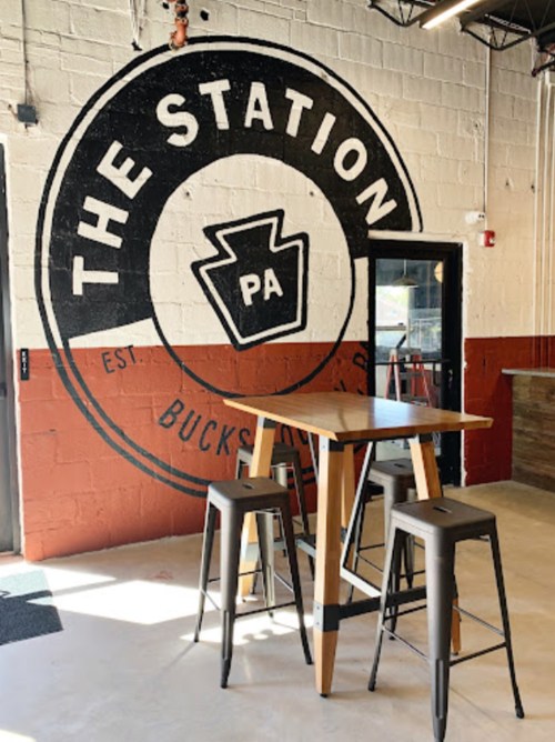 A modern interior featuring a wooden table and stools against a large mural that reads "THE STATION PA."