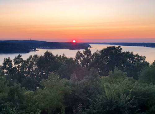 A serene sunset over a calm lake, with silhouettes of trees in the foreground and vibrant colors in the sky.