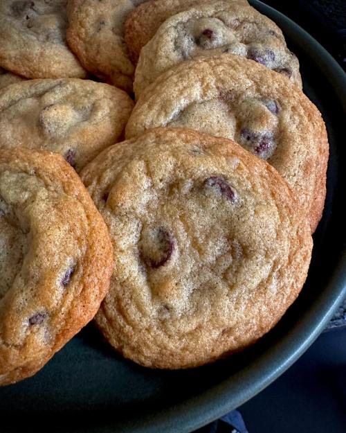 A close-up of freshly baked chocolate chip cookies on a dark plate, golden brown and slightly chewy.