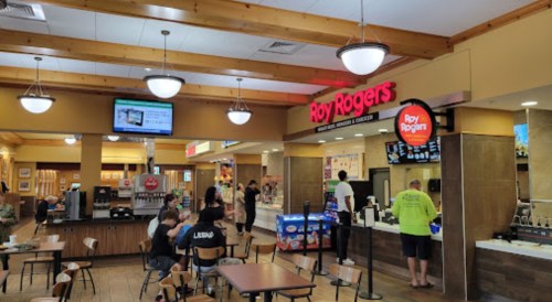 Interior of a food court featuring a Roy Rogers restaurant, with customers dining and ordering at various food stations.