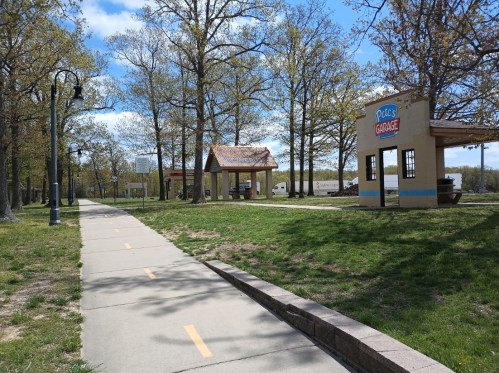 A paved path through a park with trees, leading to a small building labeled "Plaza Garage" and a gazebo.