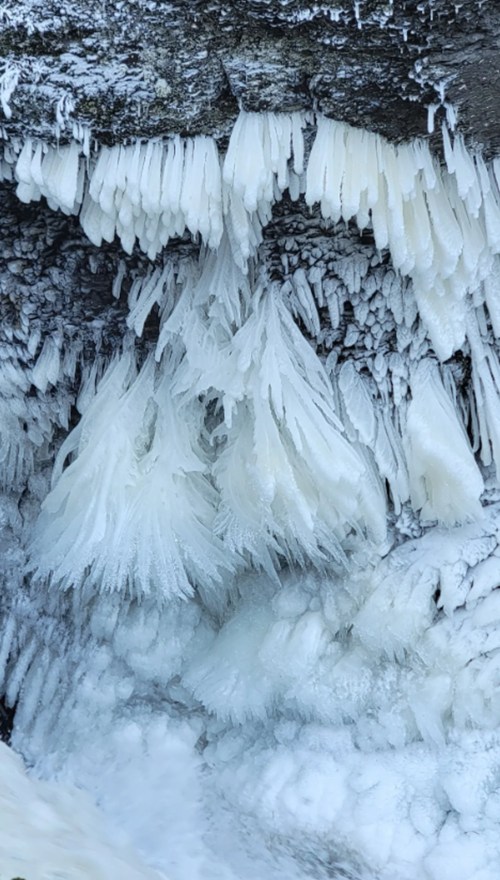 Icicles and ice formations hang from a rocky surface, creating a textured, frosty landscape.