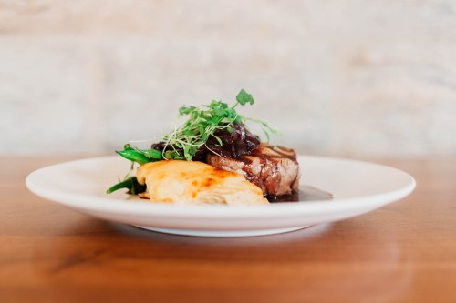 A plated dish featuring meat with sauce, green garnish, and a side of creamy potatoes on a wooden table.