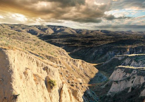 A vast, rugged landscape with rolling hills and dramatic clouds in the sky, showcasing earthy tones and textures.