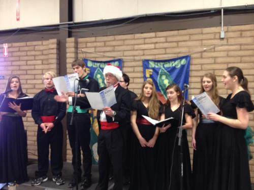 A choir of young singers in black outfits performs with music sheets in a festive setting.