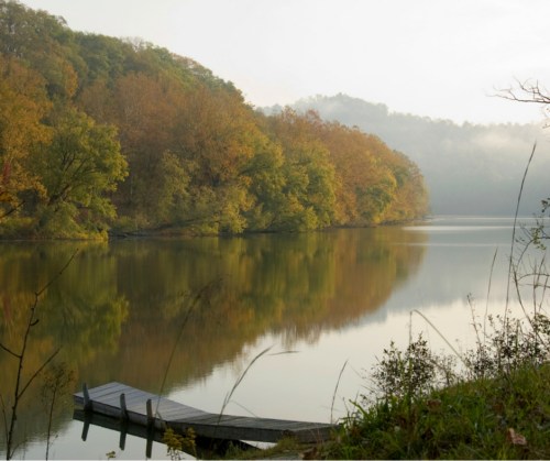 A serene lake surrounded by autumn trees, with a wooden dock extending into the calm water.
