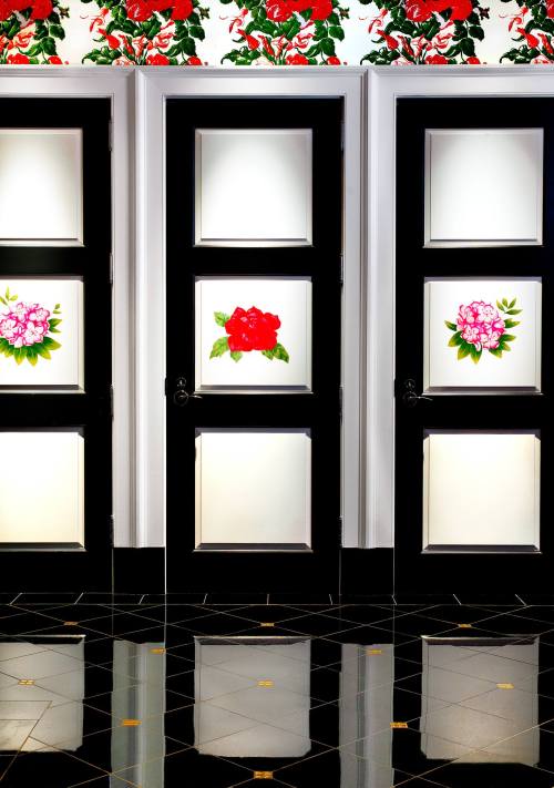 Three black doors with floral designs, set against a floral wallpaper and reflecting on a shiny black floor.