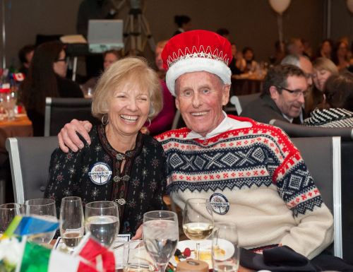 A smiling couple at a festive event, with one wearing a red and white Santa hat and a cozy sweater.