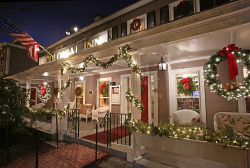 A festive inn decorated with wreaths and lights, featuring a welcoming porch and an American flag.