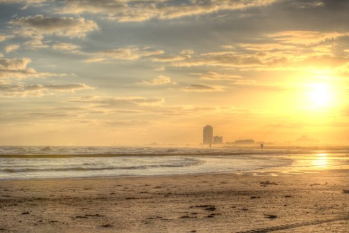A serene beach at sunset, with gentle waves and a distant skyline under a cloudy sky.