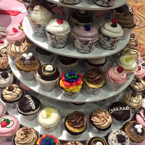 A tiered display of colorful cupcakes with various toppings and designs, arranged in an elegant presentation.
