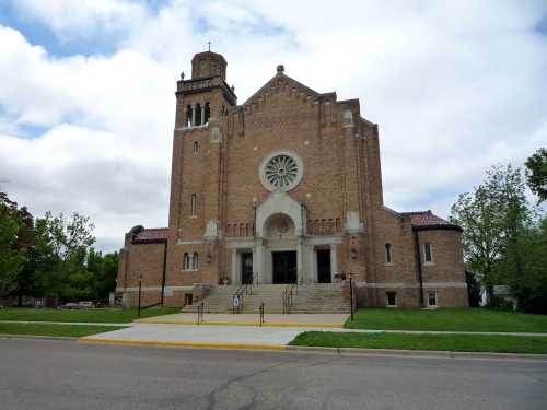 A large brick church with a prominent rose window and bell tower, set against a cloudy sky.