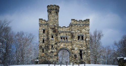A stone castle tower stands amidst snow-covered trees under a cloudy sky.